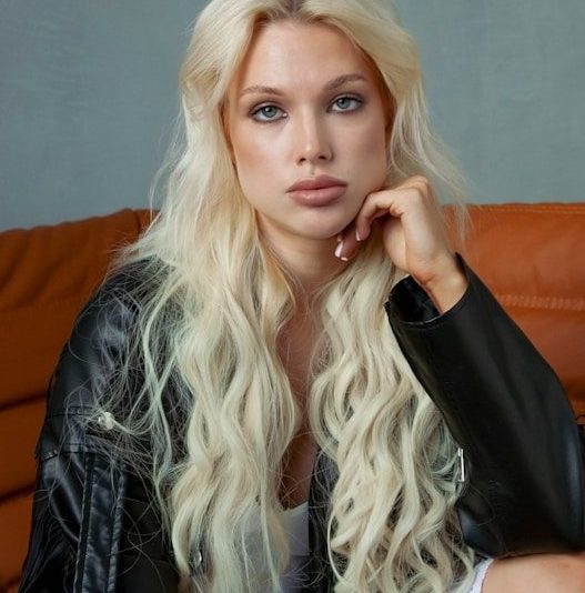 Blonde woman in leather jacket on orange couch.