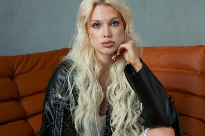 Blonde woman in leather jacket on orange couch.