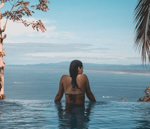 woman wearing black bikini tap swimming on body of water between trees